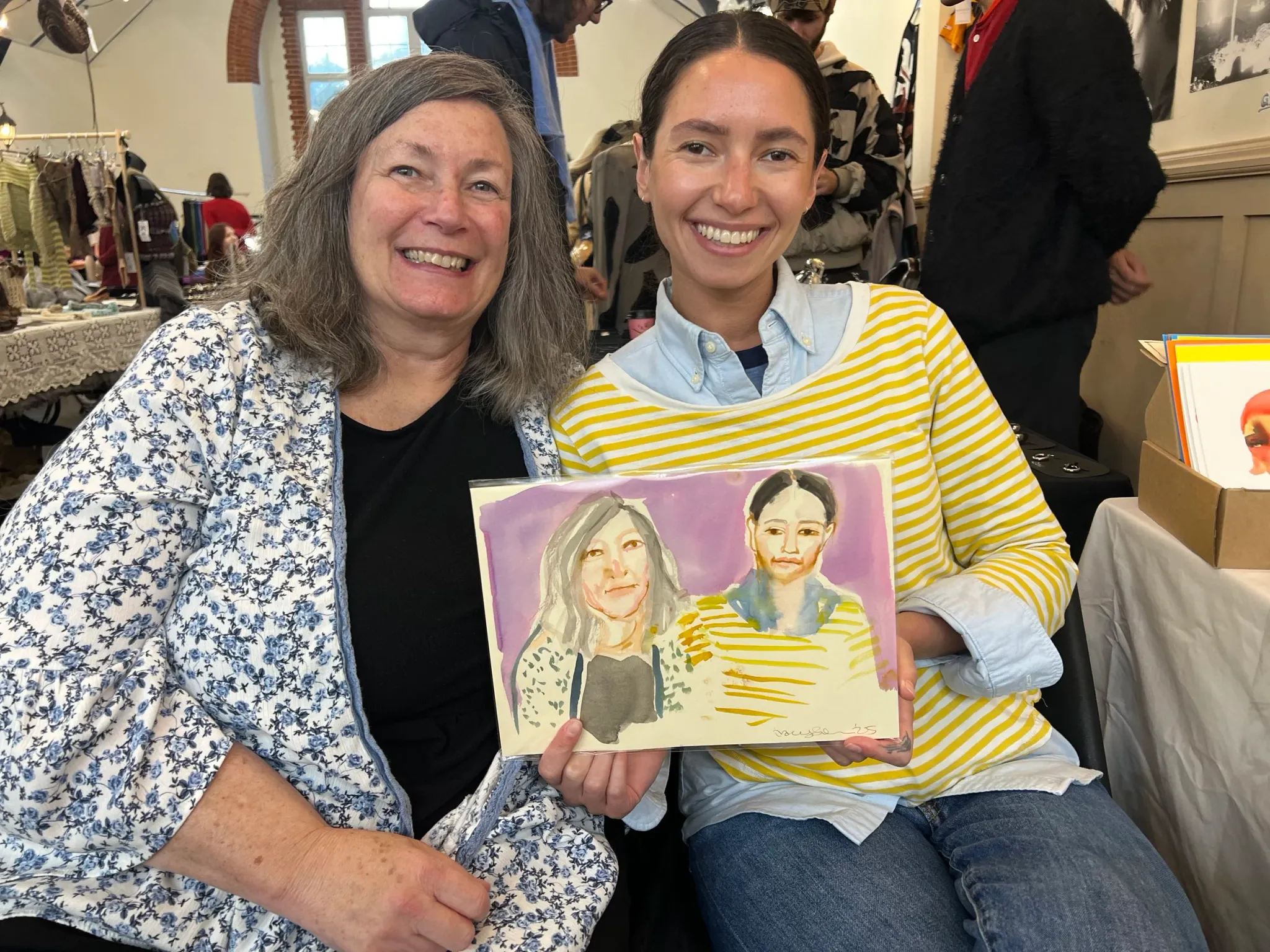 Two women holding a watercolour portrait.
