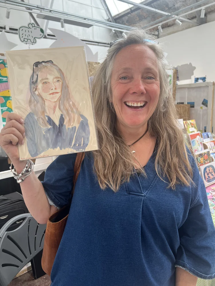 People holding watercolour portraits at event.