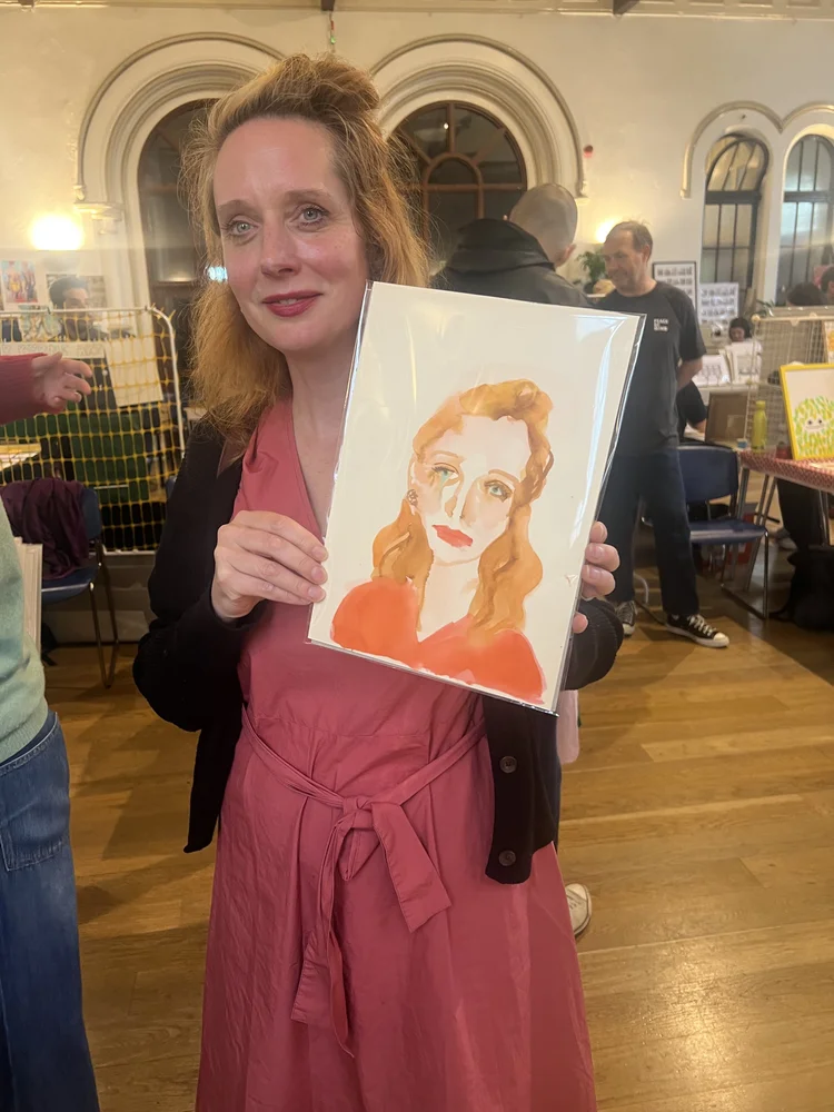 People holding watercolour portraits at event.