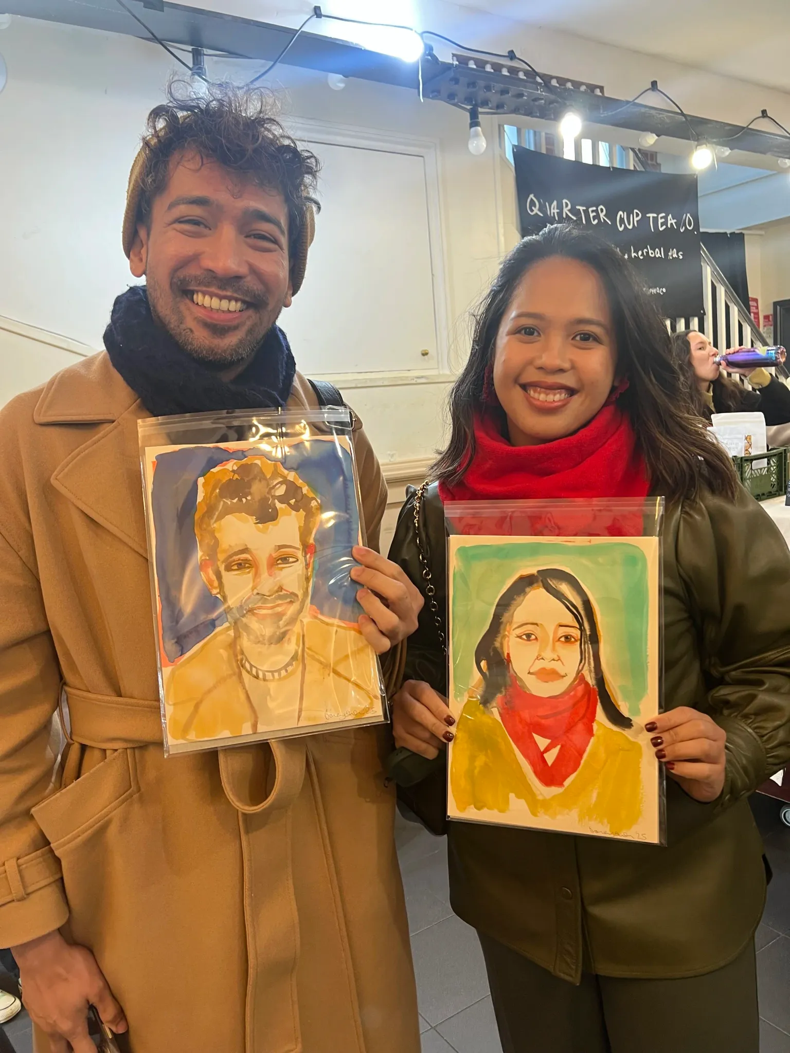 A man and woman smiling, each holding a watercolour portrait of themselves.