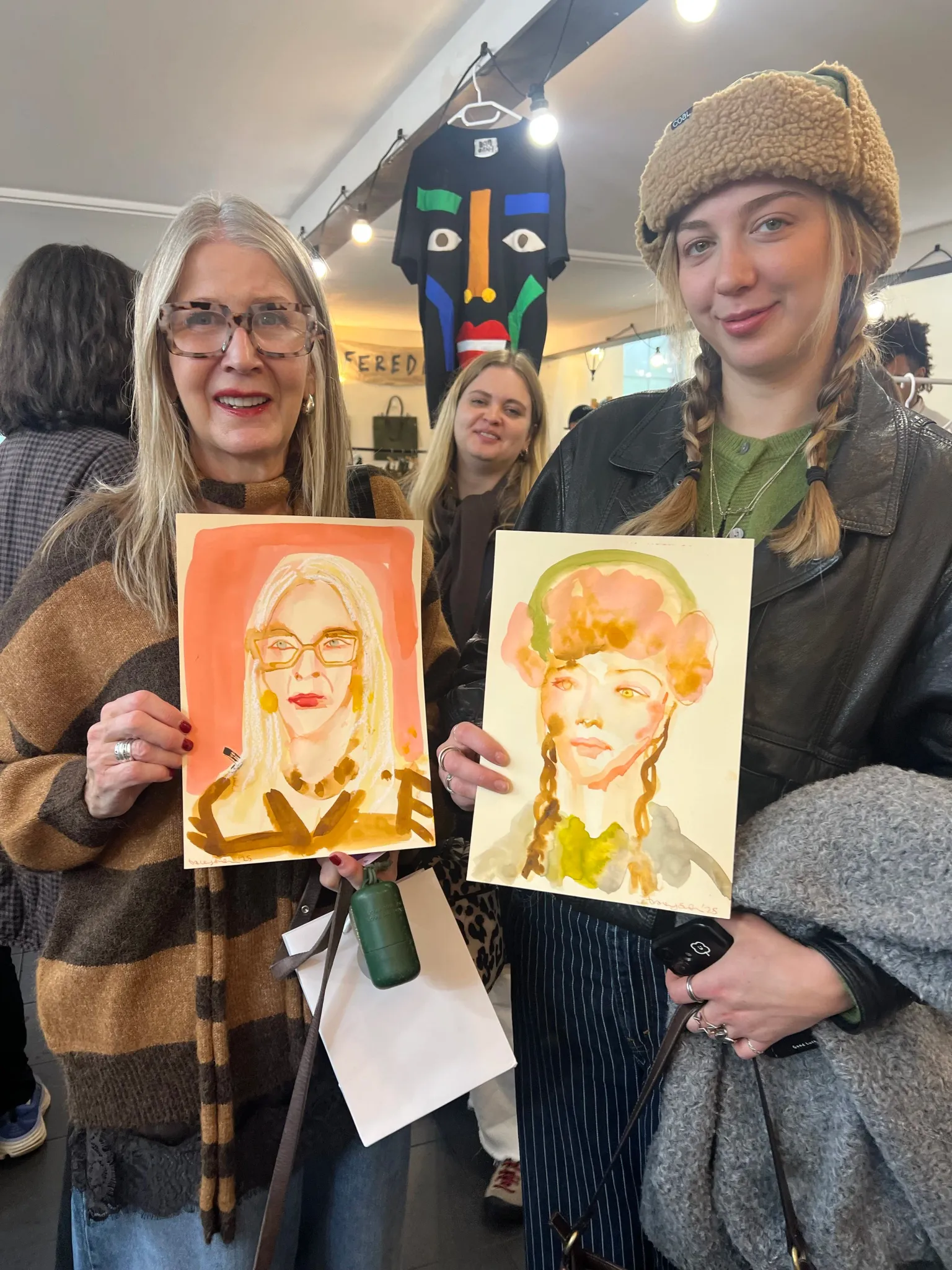 Two women holding up watercolour portraits.