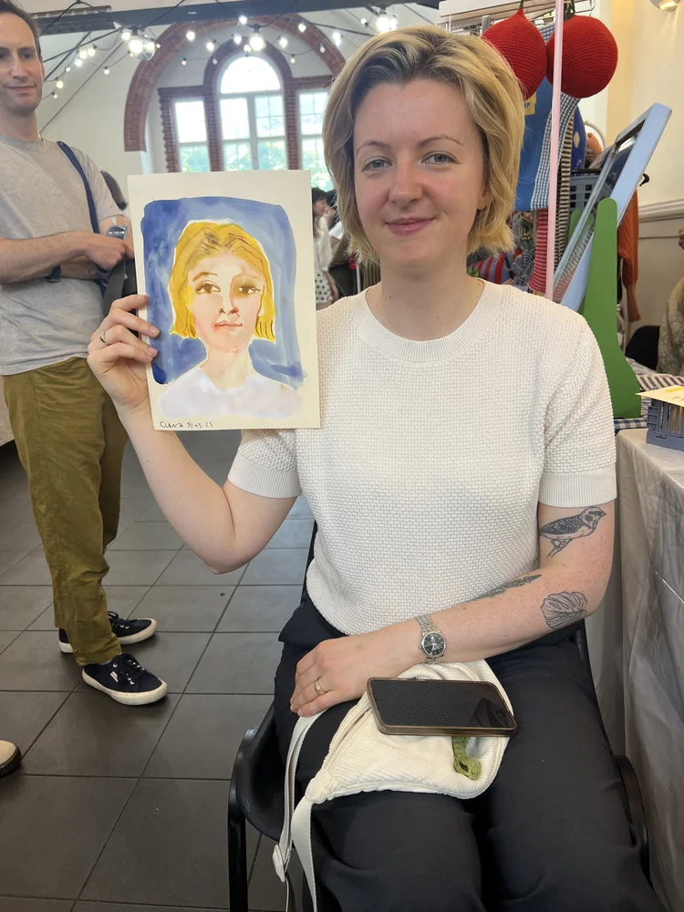 Smiling woman in white holding her watercolour portrait.