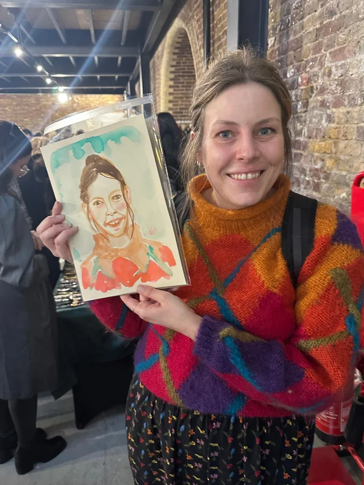 Smiling woman in colourful sweater holding portrait.