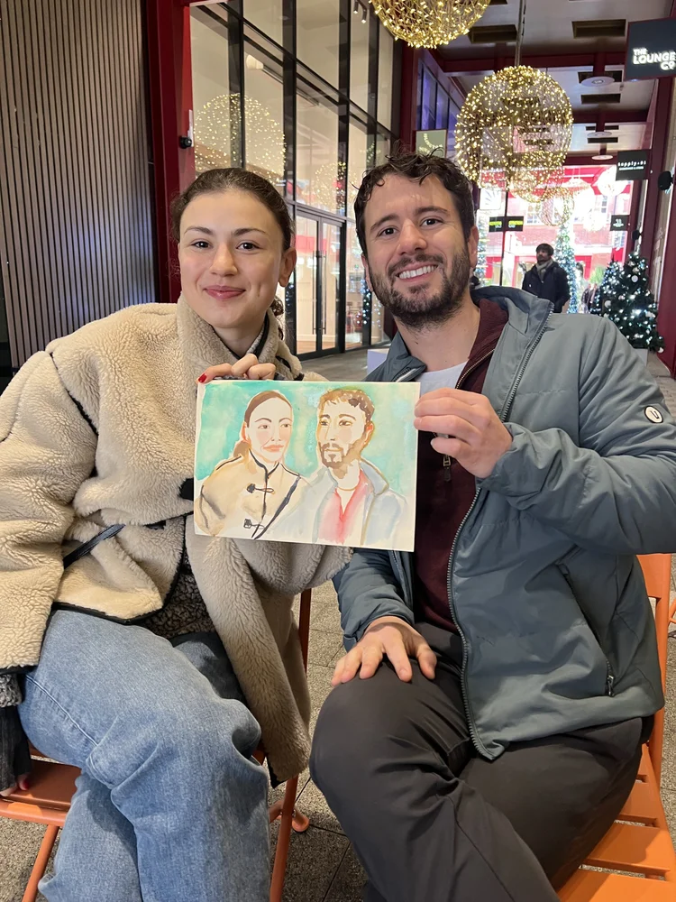 Smiling couple holding watercolour portrait.