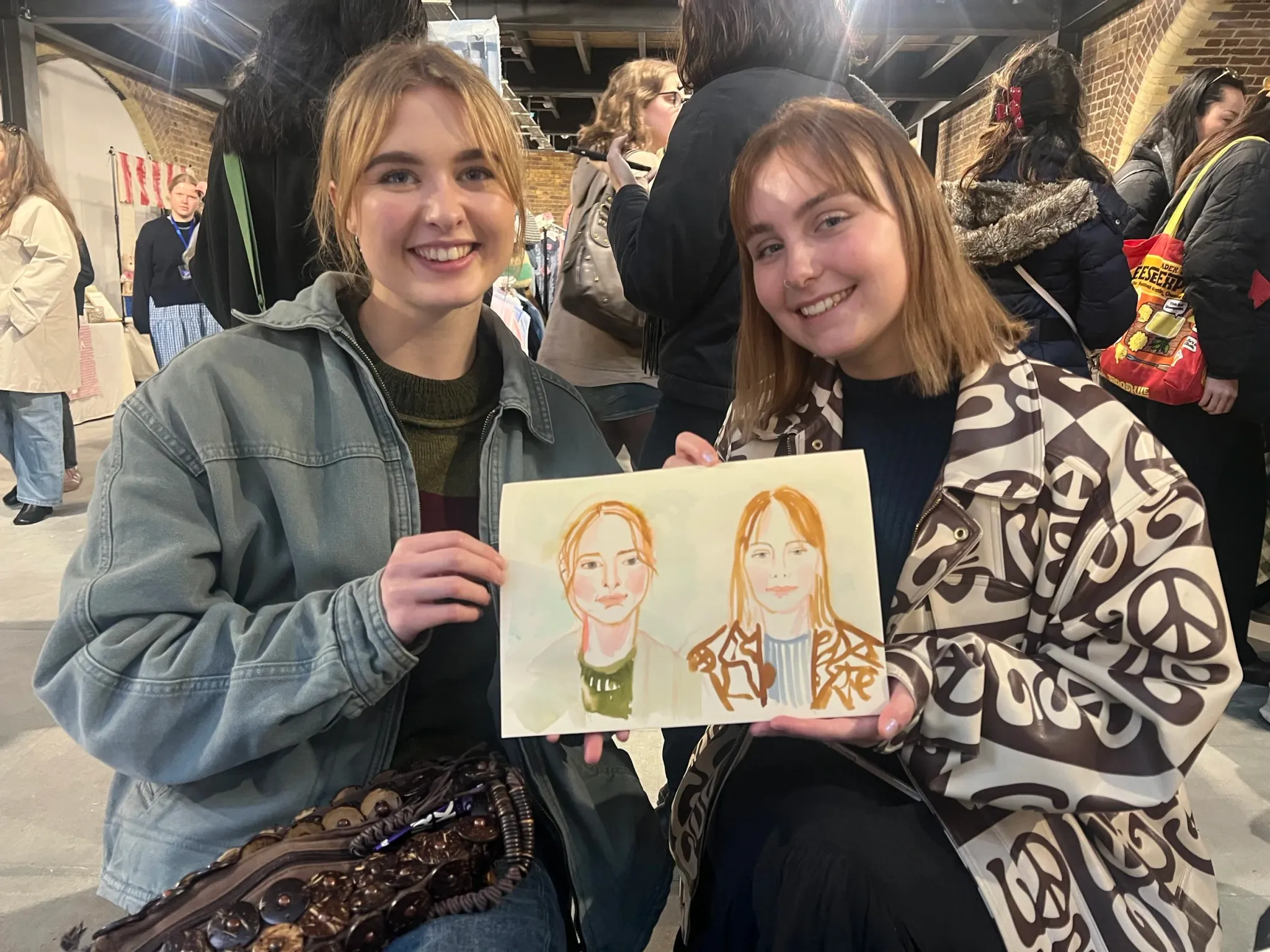 Two smiling women holding watercolour portraits.