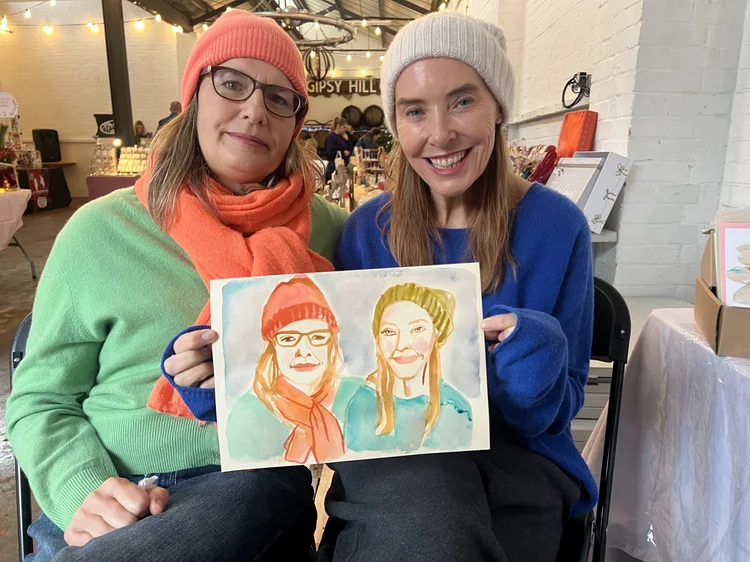 Two women holding their watercolour portraits.