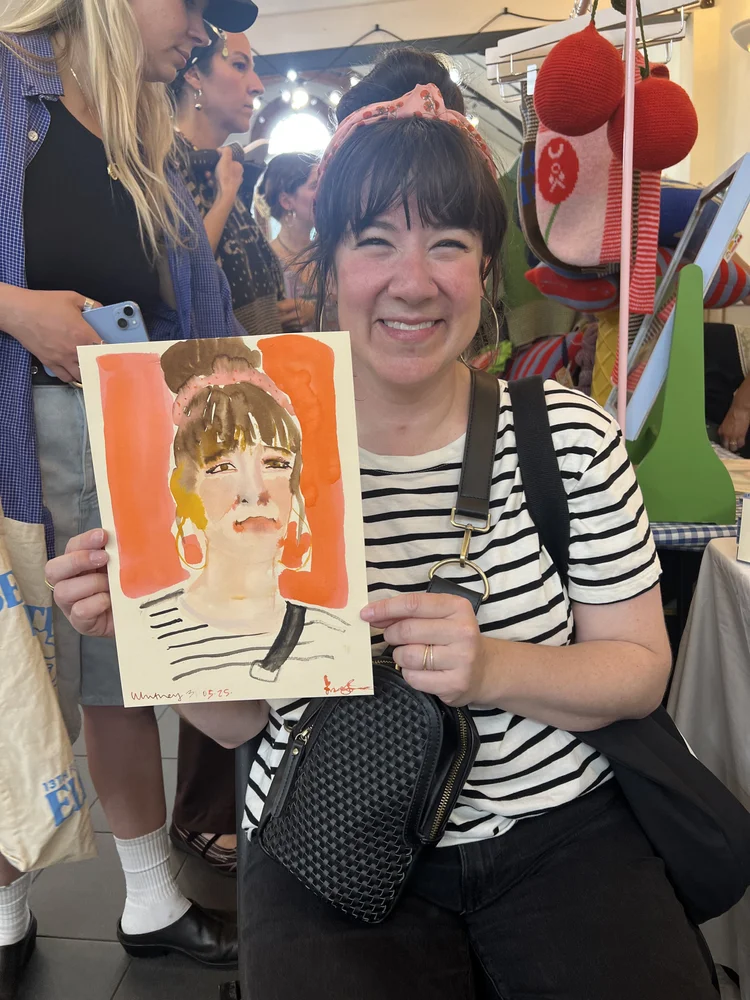 Smiling woman holding a watercolour portrait.