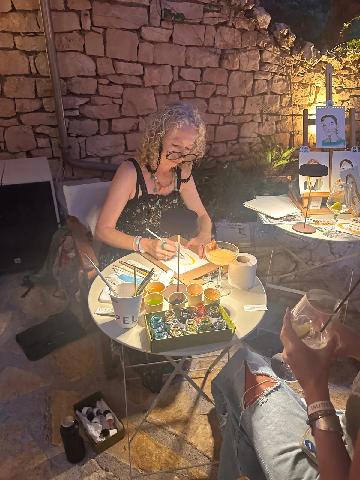 Tracey Smith painting live by candlelight at an evening event, with her Inky Faces portraits on display behind her